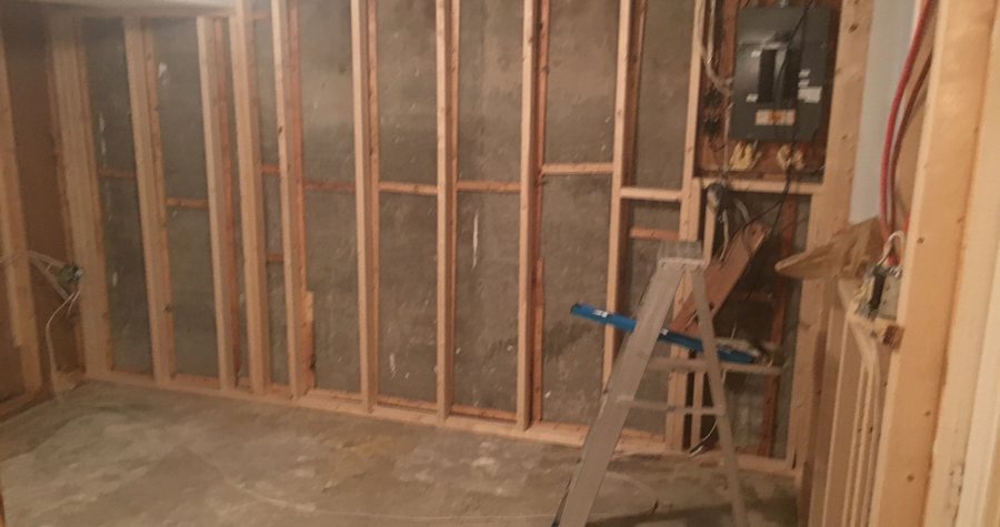 Open stud framing in a basement addition with the electrical panel relocated onto the new wall and circuits run to it.