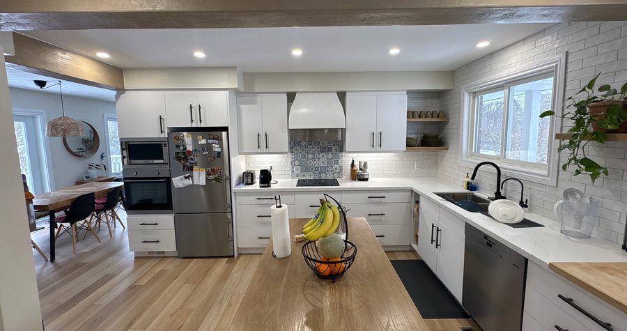 A finished, lived-in Cambridge kitchen with white cabinetry, a painted structural beam, tile backsplash and an island.