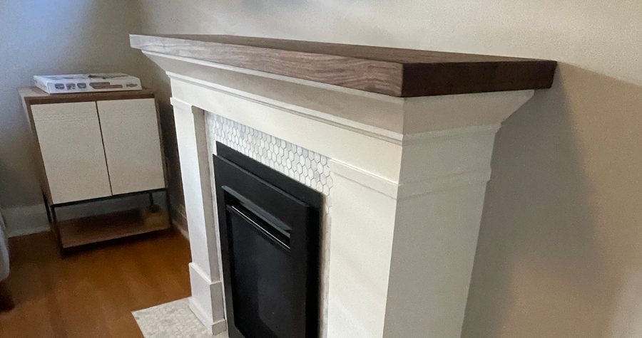A mitred corner on a built-in fireplace mantle, walnut top over a painted surround with hexagon tile.