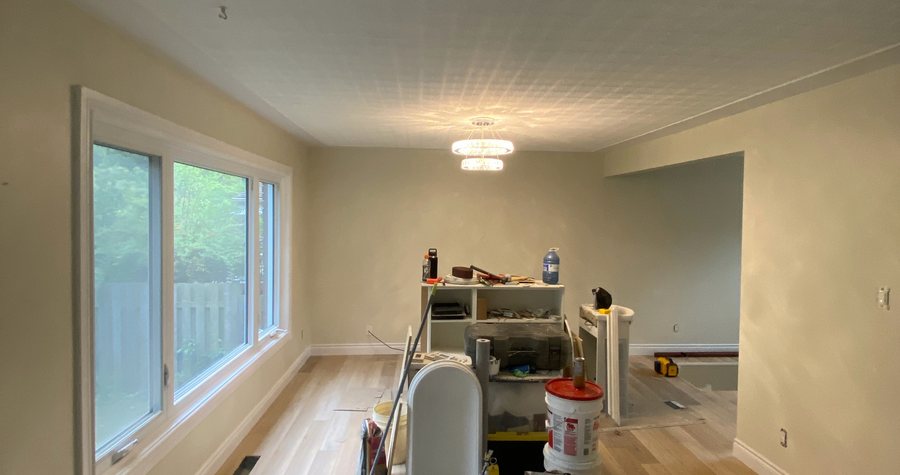 Fresh hardwood flooring installed in a hallway, with tools and finishing materials staged tidily against the wall under painter's tape.