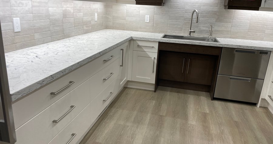 A finished kitchen, wide, with white cabinetry, quartz countertops and stainless appliances.