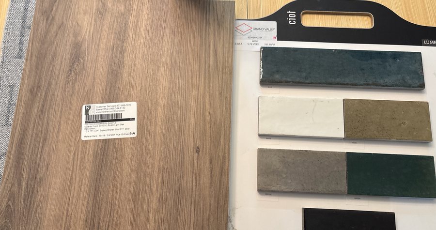 A cabinet door sample and a board of glazed tile swatches with per-square-foot pricing laid out on a job-site table.