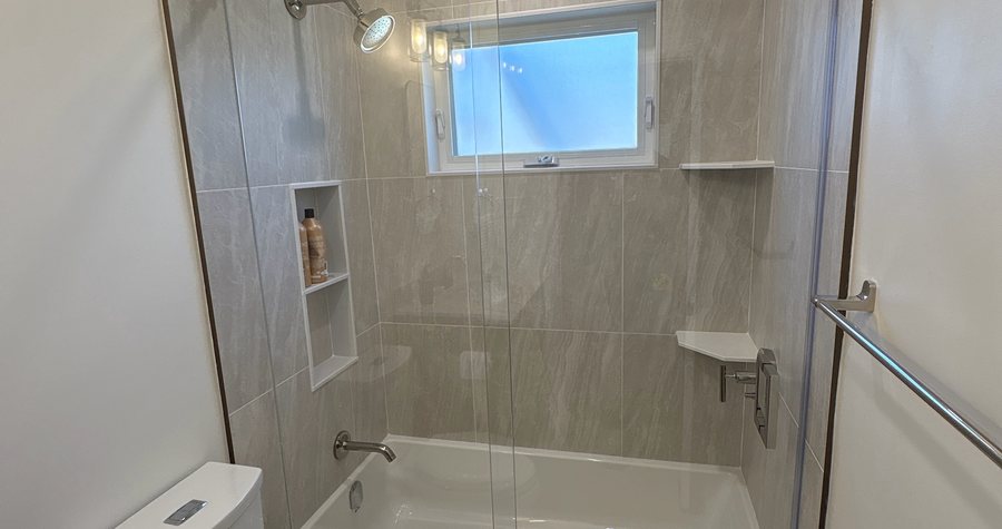 A finished curbless glass shower with full-height stone-look tile, a rain head and a built-in niche.