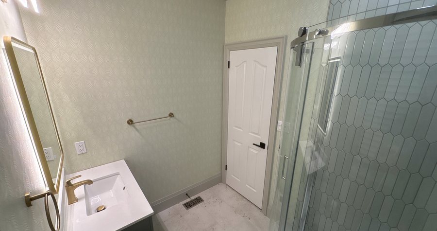 A finished ensuite with green hexagon tile in the glass shower and a brushed-brass faucet on the vanity.