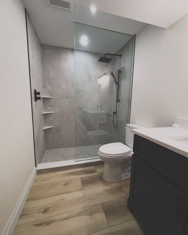 Full bathroom with frameless glass shower, tiled niche and wood-look flooring