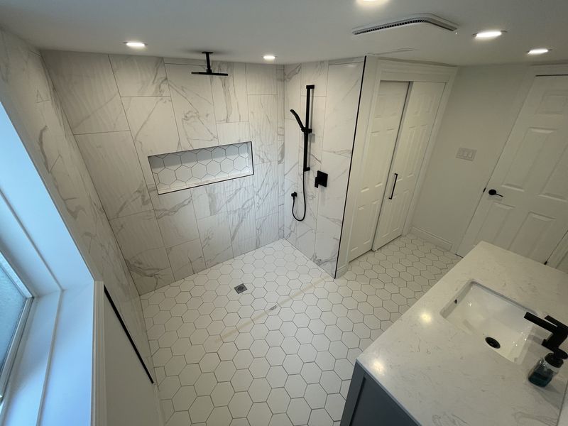 Marble-tiled walk-in shower with hexagon floor tile and matte black fixtures