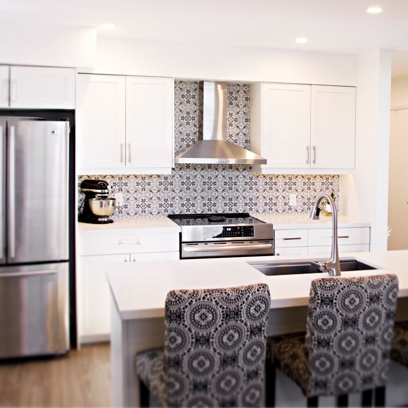 White kitchen with a patterned tile backsplash and stainless hood