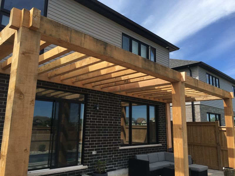 Cedar pergola over a stone patio against a brick exterior