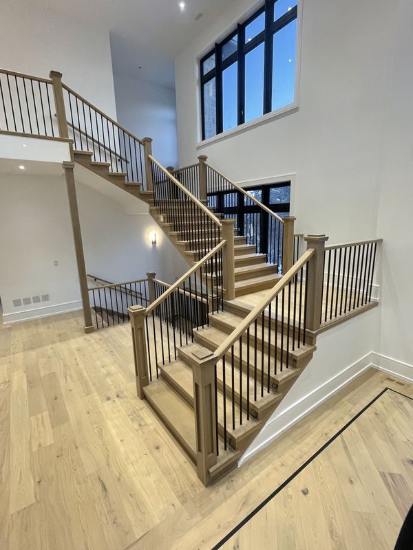 Open staircase beside a two-storey window wall in white oak